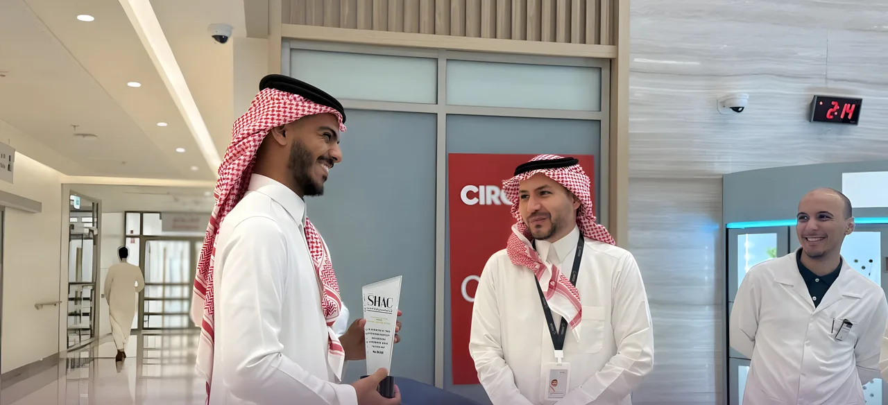 أحد المشاركين في الزيارة يحمل درع SHAC مبتسمًا في مستشفى الصبح