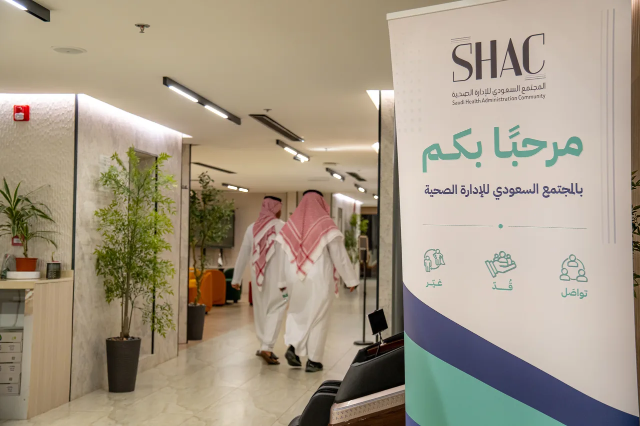 لوحة «مرحبًا بكم بالمجتمع السعودي للإدارة الصحية» في ممرّ مكان اللقاء، وحاضران يمشيان في الممر