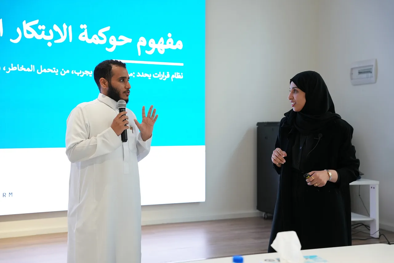 مشارك يتحدث بالميكروفون إلى جانب المتحدثة أمام شريحة حوكمة الابتكار الصحي