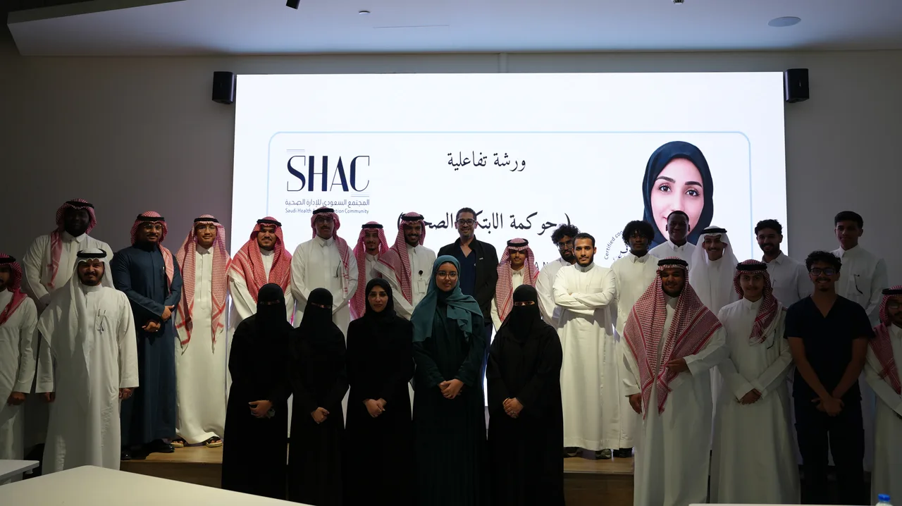 صورة جماعية للمشاركين أمام شاشة الورشة التفاعلية «حوكمة الابتكار الصحي»