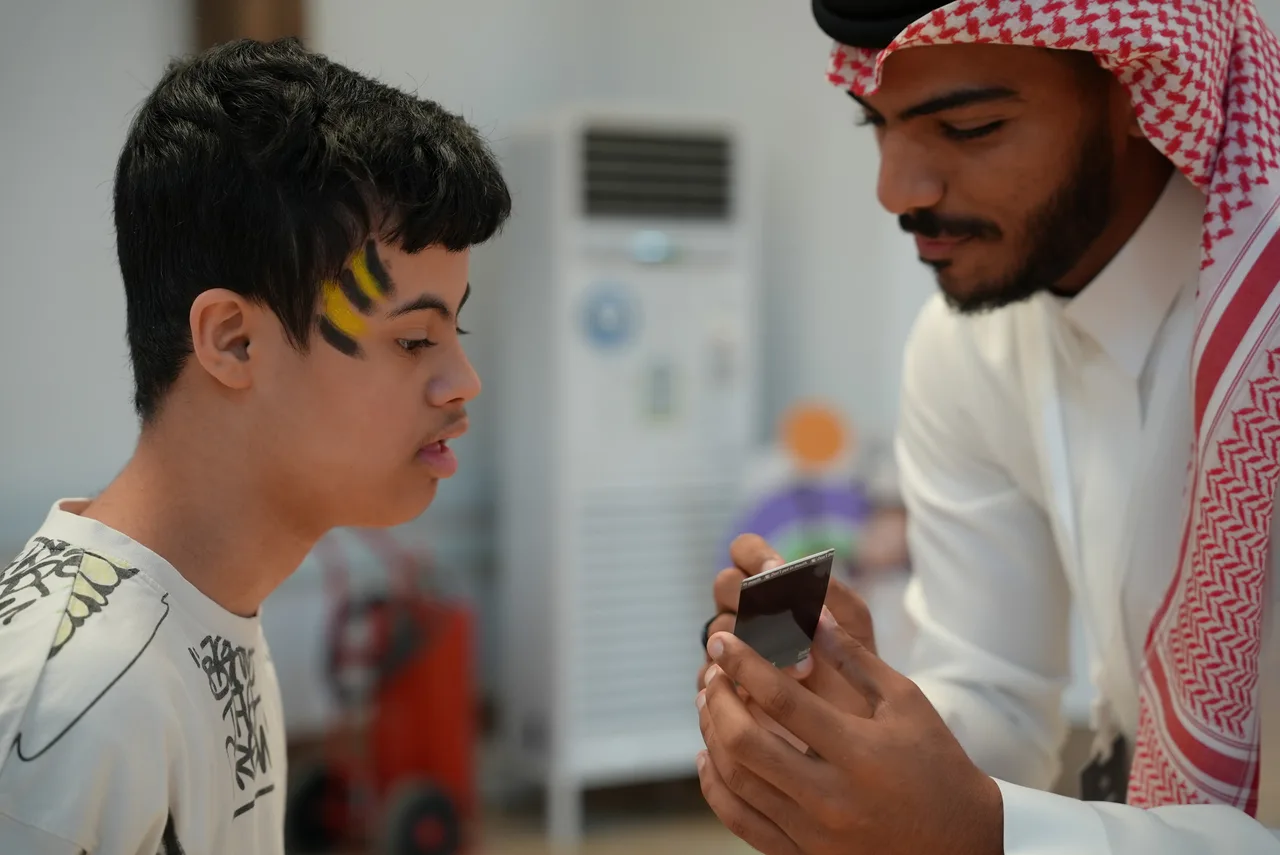 متطوع يُري طفلًا رسمة وجهه على شاشة الهاتف
